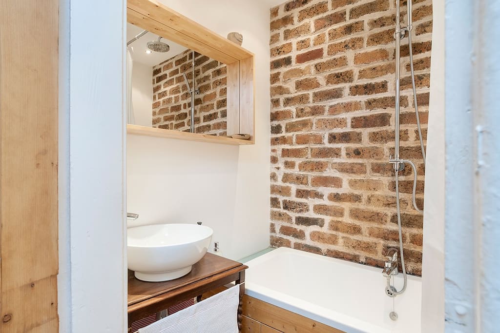 Contemporary bathroom with rain shower over bath, feature stone wall and underfloor heating